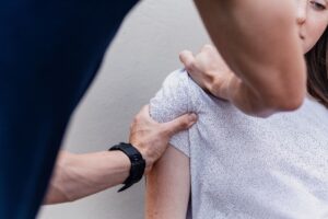 A physical therapist manually manipulates a woman's shoulder.
